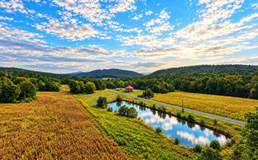 Aerial view of open fields, a farm pond and wooded mountain ridges at Pine Grove Road.
